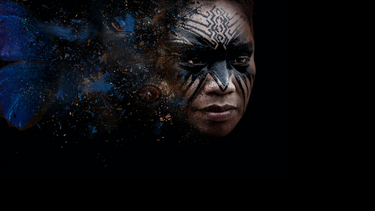 A dark image of a young woman in ceremonial blue make up, particularly around the eyes, looking to the left, reminiscent of an amazonian shaman