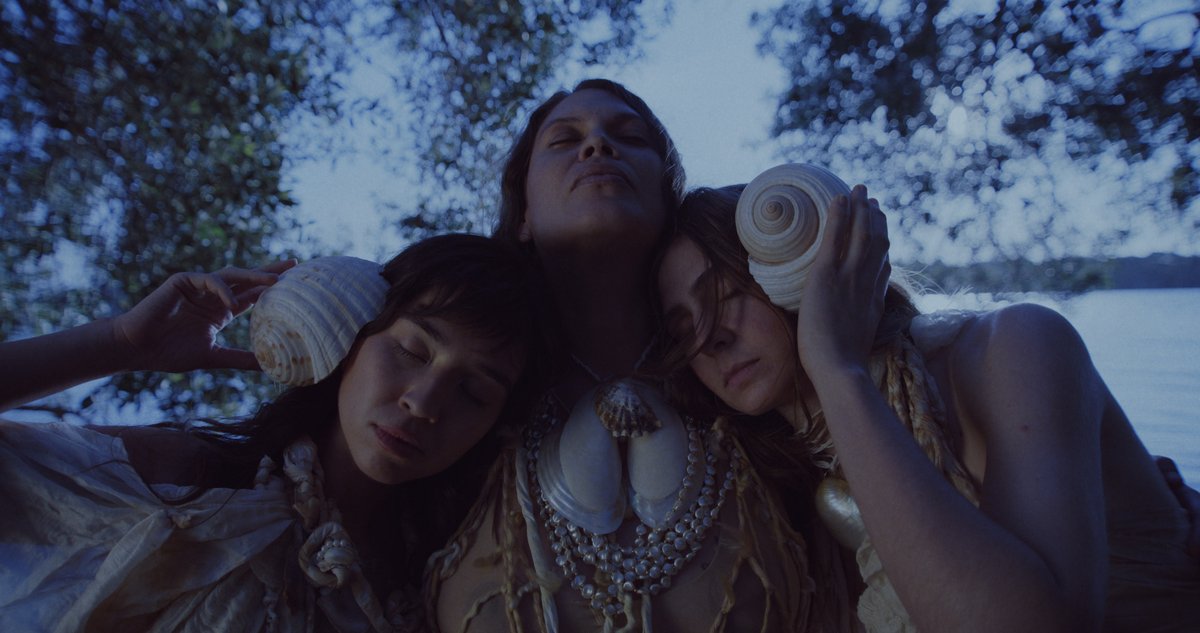 An upward shot of three women holding each other and looking to the sky at night