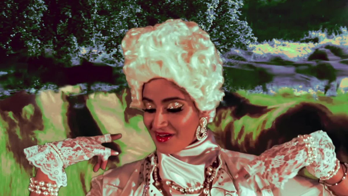 A woman of indian descent wearing a costume like that of the french aristocracy, frilly clothes and a platinum wig, looking down mid song with a undulating background of green and blue that hints at a landscape