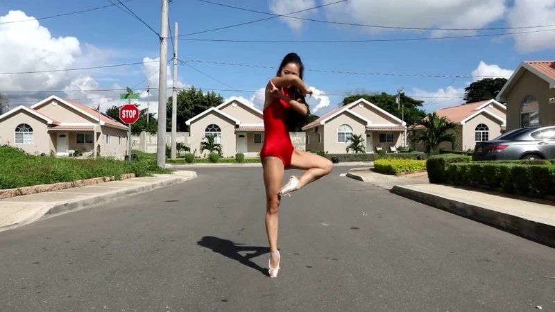 An image of an Asian woman in a red outfit dancing in the middle of a suburban street