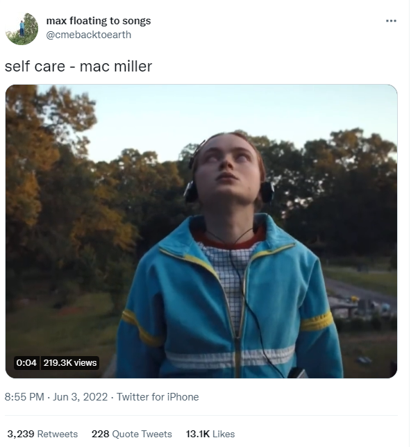 A screenshot of a tweet of a young girl in a blue jacket, with red hair, in a cemetery looking up at the sky with headphones on. The tweet caption reads self care by mac miller