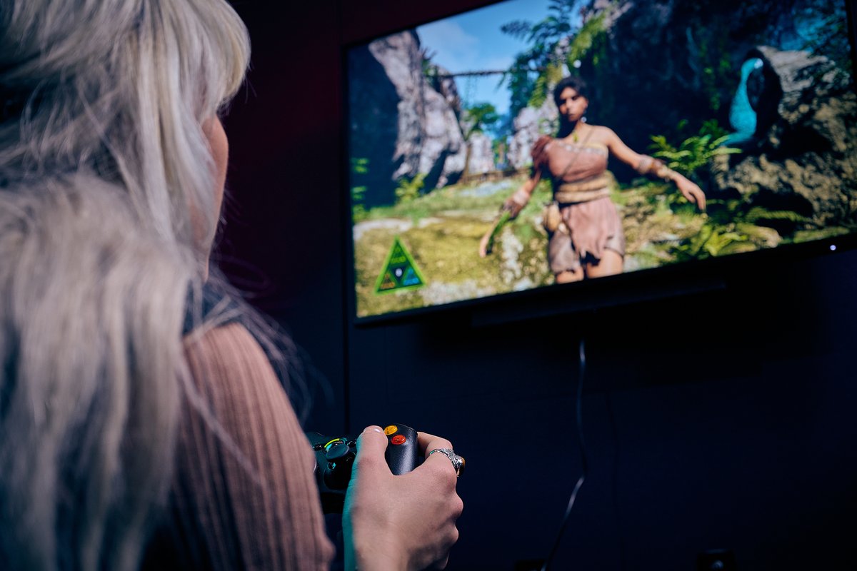 A close up image of a woman playing a videogame, on the screen it looks like a maori warrior