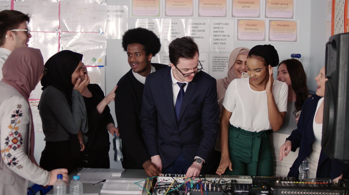 A diverse group of students gathered around DJ decks, having a good time.