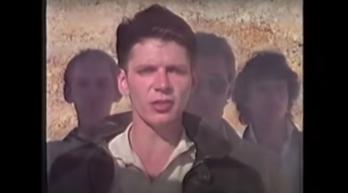 A 4:3 ratio image of a blurry white man singing with other faces in the background in a still from Great Southern Land by Icehouse.