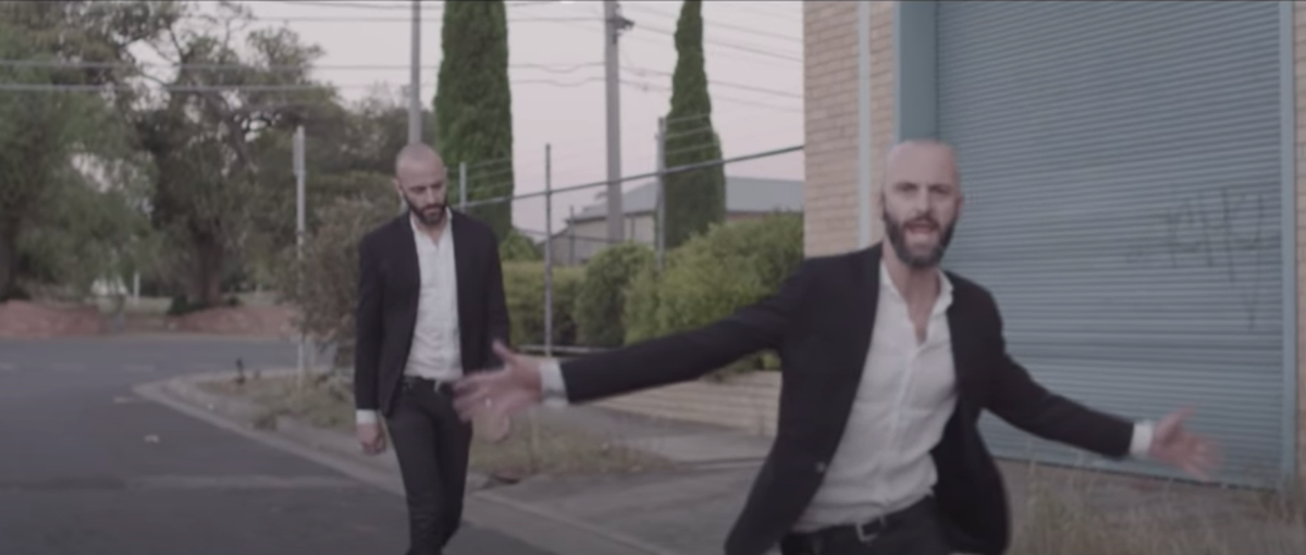 An image of a man in a black suit and white shirt walking down a suburban street with one version of himself slightly ahead
