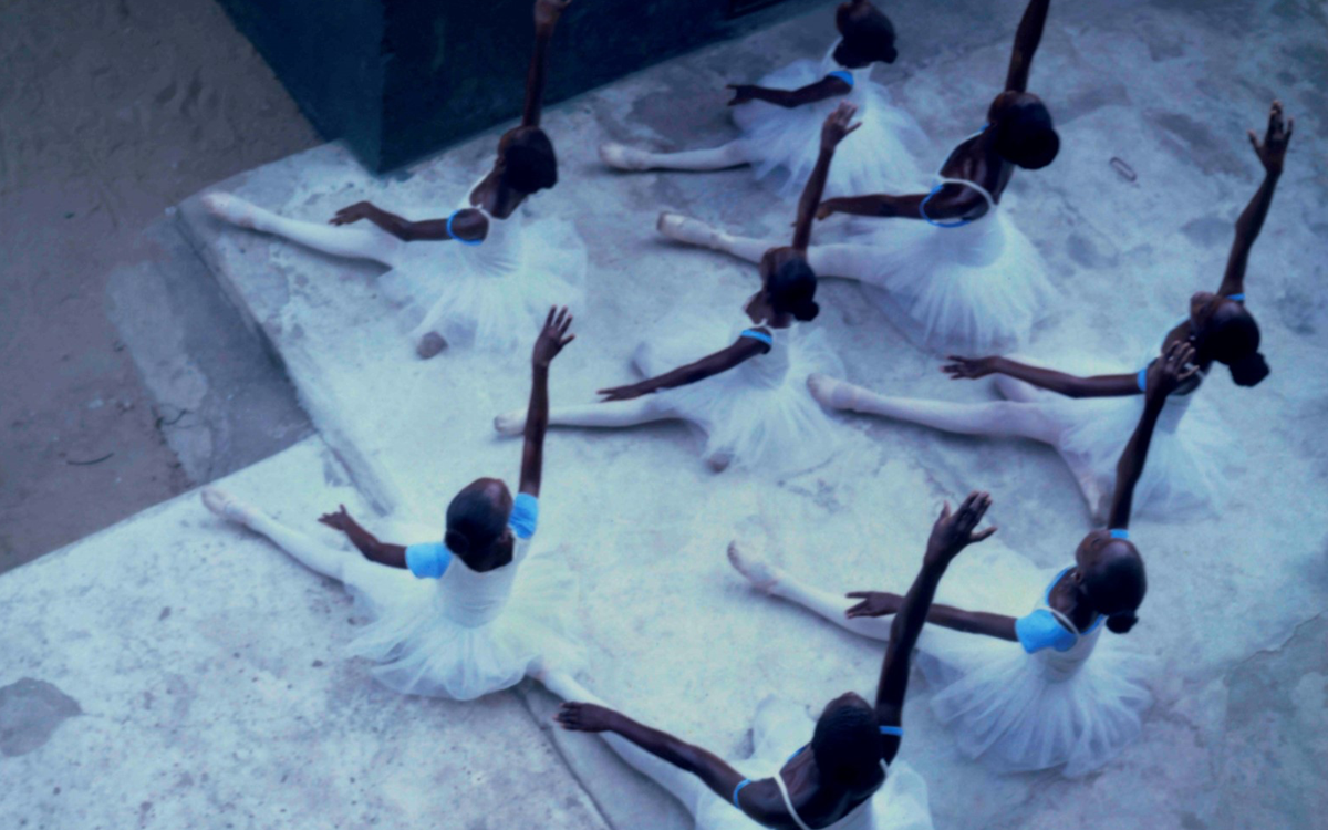 An overhead view of a group of Nigerian ballet dancers with their arms outstretched and their shadows cast against a concrete background