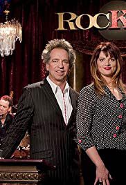A picture of a man and a woman standing in front of a curtain, the man in a suit and the woman in a sparkly top